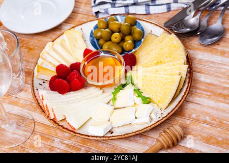 Différents types de fromage, miel, framboises et olives sur bois Banque D'Images