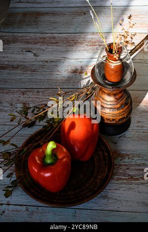 Poivrons rouges sur une plaque d'argile, branches de rose sauvage et un vase en bois avec des fleurs séchées Banque D'Images