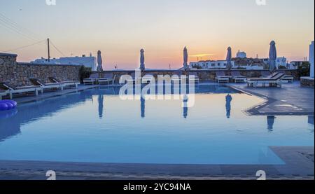 Une piscine typique à Mykonos à côté d'un petit hôtel est l'une des îles grecques pendant le coucher du soleil et l'avion a fait un cercle pour atterrir à l'aéroport de Mykonos Banque D'Images