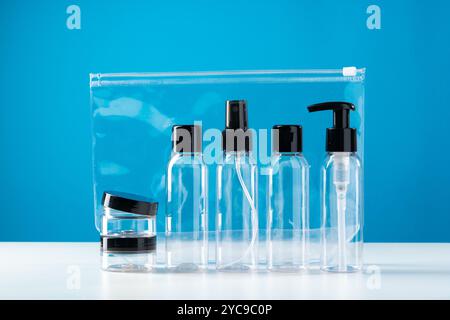 Trousse de toilette transparente contenant divers contenants de voyage sur fond bleu vif Banque D'Images
