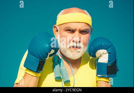 Drôle d'homme barbu debout dans la posture de boxe. Homme âgé frappant le sac de frappe. Boxe. J'adore la boxe. Portrait d'un boxeur senior déterminé sur bleu Banque D'Images