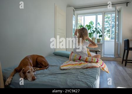 Femme s'étirant dans le lit pendant que le chien attend, profitant d'un matin lent et conscient et détendu début de la journée Banque D'Images