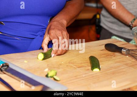 Une femme noire africaine dans une cuisine montrant ses mains couper un concombre sur une table de cuisine en bois Banque D'Images