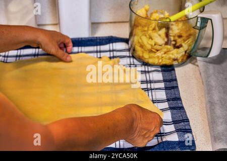 Retirer la pâte traditionnelle à la main sur la serviette à carreaux, bol avec des tranches de pomme sur la table de cuisine. Pâte de préparation pour strudel. Banque D'Images