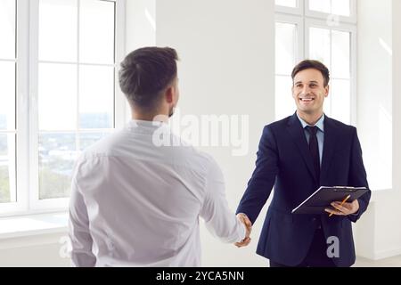 Homme agent immobilier debout dans de nouveaux appartements avec contrat signé serrant la main avec le client Banque D'Images