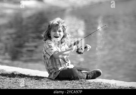 Drôle de pêche de petit enfant heureux le week-end. Un garçon de pêcheur se tient dans le lac avec une canne à pêche et attrape du poisson. Banque D'Images