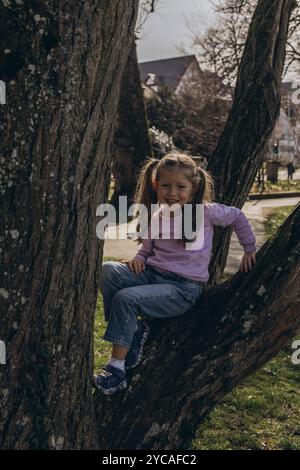 Une petite fille est montée dans un arbre, profitant d'un moment ludique à l'extérieur. Photo de haute qualité Banque D'Images