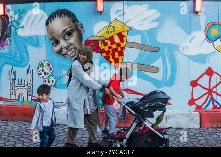 Angleterre, Londres, Southwark, Muslim Lady avec des enfants marchant devant le panneau d'affichage coloré Banque D'Images