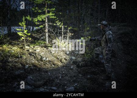 Un individu navigue soigneusement dans une forêt sombre la nuit, en utilisant une lampe de poche pour éclairer le chemin parmi les arbres et le terrain, cherchant à découvrir hi Banque D'Images