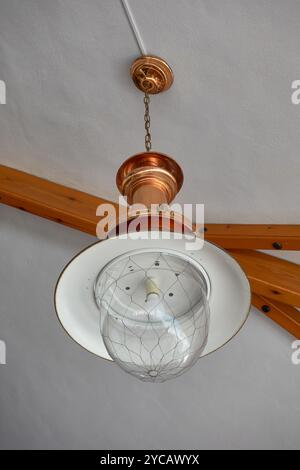 Un plafonnier vintage en cuivre avec un abat-jour globe en verre pend à un plafond blanc. Poutres en bois sont visibles, créant un rustique mais élégant dans Banque D'Images