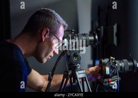 Caméraman masculin adulte Configuration des caméras pendant une diffusion en direct dans un studio de télévision, vue latérale Banque D'Images