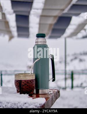 Termo et mate sur une table en bois avec de la neige, sous un auvent, un après-midi d'hiver. Coutume Argentine typique Banque D'Images