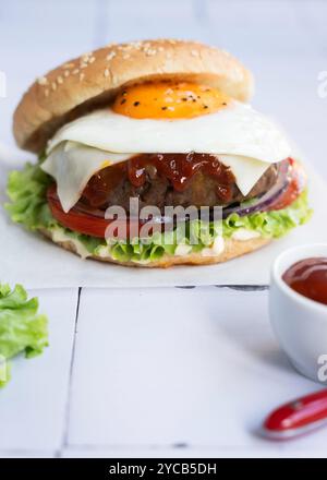 Un hamburger gourmand délicieux et visuellement appétissant garni d'un œuf frit, de fromage suisse, d'oignons, de laitue fraîche, de tomate, et un pain brillant aux graines de sésame, Banque D'Images