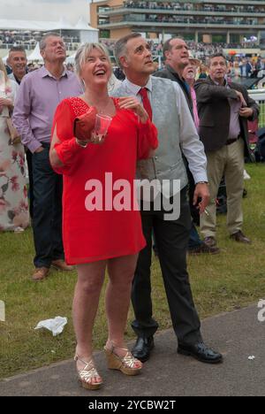 Heureux, riant souriant une femme parieuse avec son partenaire regardant les courses de chevaux sur un grand écran extérieur. Ils sont sur la Heath, qui est le côté libre de l'hippodrome. Je dirais que son cheval gagne, son mari partenaire n’a pas l’air si heureux. Regard contrasté sur leurs visages. Ascot, Berkshire, Angleterre 18 juin 2016 2010s UK HOMER SYKES Banque D'Images