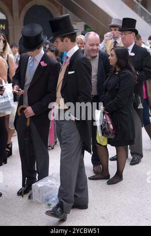 Faisant la queue, les gens font la queue pour acheter un billet de train à un distributeur automatique. Groupe de jeunes hommes qui vont à Royal Ascot portant des chapeaux et des manteaux de queue de code vestimentaire. Ils ont l'air différents des gens ordinaires dans la file d'attente. Gare de Waterloo Londres, Angleterre 22 juin 2012 2010s UK HOMER SYKES Banque D'Images