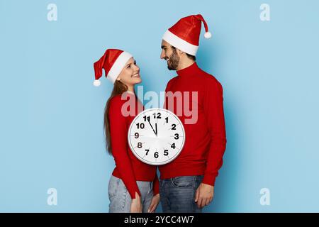 Couple portant des chapeaux de Noël sourit avec une horloge le jour de fête Banque D'Images