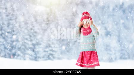 Enfants jouant avec la neige en hiver. Petite fille en veste colorée et chapeau tricoté attrapant flocons de neige dans le parc d'hiver à Noël. Banque D'Images