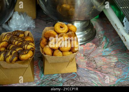 Les mini beignets assortis sont soigneusement disposés dans des plateaux en papier, présentant différentes garnitures comme le chocolat et le sucre, sur une nappe vibrante dans un buste Banque D'Images