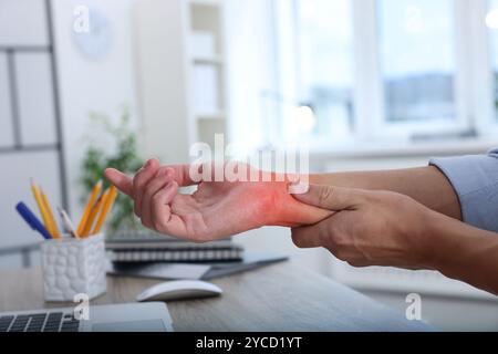 Homme souffrant de douleur au poignet à la table en bois, gros plan. Travail de bureau, syndrome du canal carpien Banque D'Images