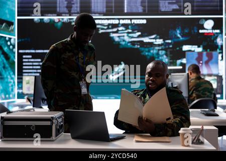 Un groupe de soldats dans un environnement de bureau collabore à l'analyse du renseignement, à l'interprétation des données et à la planification stratégique pour maintenir la sécurité nationale. Équipage militaire de contrôle de drones. Banque D'Images