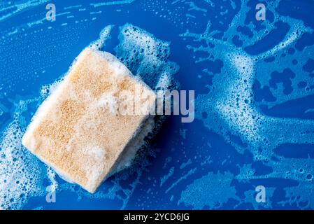 éponge en mousse pour laver la vaisselle sur une table en céramique bleue avec espace de copie. Éponge de nettoyage sur surface mouillée Banque D'Images