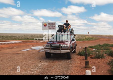 Un voyageur se détend au sommet d'un véhicule au panneau d'accueil pour le territoire du Nord, entouré par le vaste paysage de l'Outback. Le paysage est charac Banque D'Images