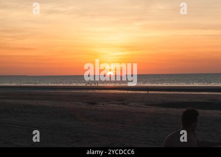 Le soleil se couche magnifiquement sur l'océan à Darwin Beach, projetant des couleurs vives à travers le ciel. Les visiteurs apprécient l'atmosphère sereine que le jour vient Banque D'Images