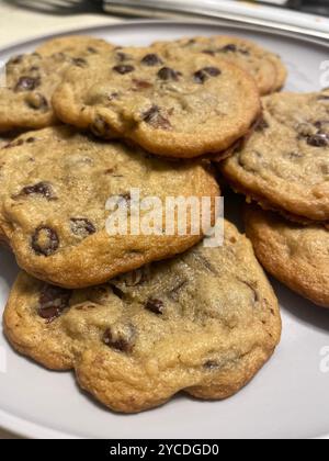 Les biscuits chauds aux pépites de chocolat de couleur dorée s'empilent de façon décontractée, leurs bords vifs et leurs morceaux fondus saisissent la lumière dans une ambiance chaleureuse et familiale. Banque D'Images