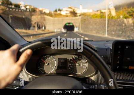 Vue du conducteur sur le compteur de vitesse, la main sur le volant. Route floue avec tunnel. Île de Madère, Portugal. Banque D'Images