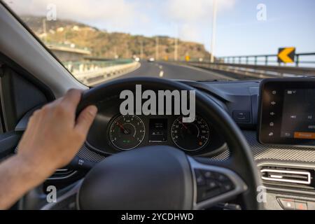 Vue du conducteur sur le compteur de vitesse, la main sur le volant. Pont routier flou. Île de Madère, Portugal. Banque D'Images