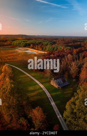 Une grange rustique se trouve le long d'une ruelle de culture de gravier qui coupe à travers une clairière dans les bois. La forêt nationale de Hoosier l'entoure de minces nuages au-dessus Banque D'Images