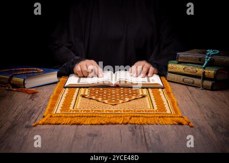 Un garçon musulman asiatique est assis et lit le Coran à la table en bois de sa maison pendant la nuit pendant le mois de ramadan, calligrap arabe Banque D'Images