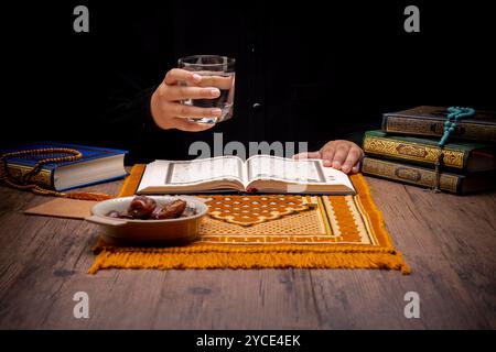 Beaucoup de palmiers dattiers sont sur des bols, des assiettes et des tasses d'eau, et le Coran est sur des tables en bois, pour attendre le temps de l'iftar, avec le concept de ramadan Banque D'Images