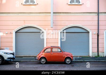 Cremona, Lombardie, Italie 15 octobre 2024 Une petite Fiat vintage rouge 500 est garée dans une rue calme devant un immeuble résidentiel rose pastel Banque D'Images