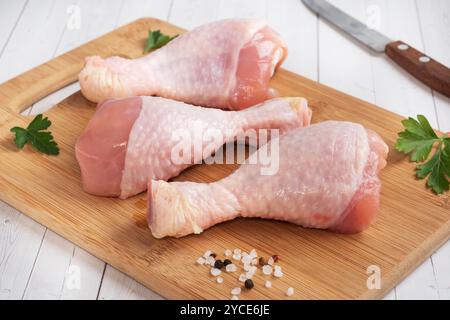 Pilons de poulet crus avec persil et épices sur un bois Planche à découper Banque D'Images
