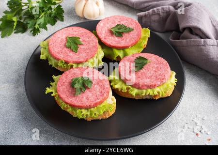 Sandwichs avec feuilles de laitue et saucisse de salami tranchée sur assiette noire Banque D'Images