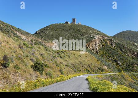 Une ruine abandonnée trône sur une colline verte sous un ciel bleu vif. Une route serpente à travers le paysage fleuri, Grigorakis Tower, entre Mar Banque D'Images