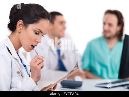 Jeune médecin asiatique pensant avec le stylo, d'autres flous derrière Banque D'Images