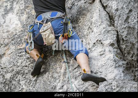 Gros plan d'un grimpeur avec de l'équipement sur une ceinture, grimpant un mur rocheux. Banque D'Images