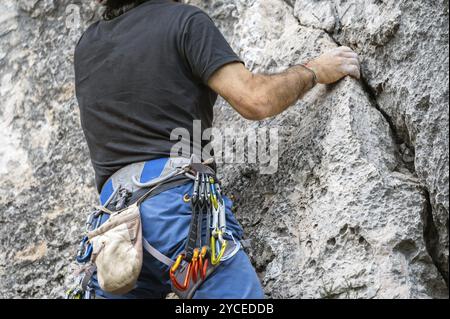 Gros plan d'un grimpeur avec de l'équipement sur une ceinture, grimpant un mur rocheux. Banque D'Images