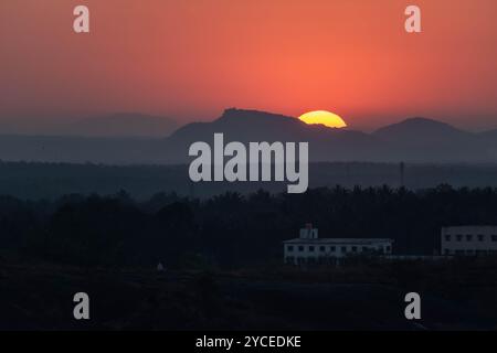 Le soleil plonge sous les montagnes projetant une lueur orange chaude à travers l'horizon tandis que les bâtiments se silhouent dans le ciel crépusculaire. Banque D'Images