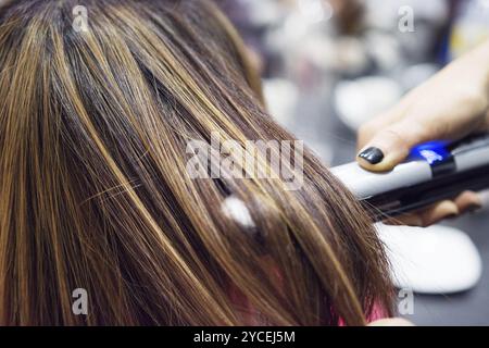 Coiffure en utilisant Hair Straightener sur brown-haired woman Banque D'Images