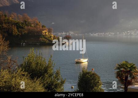 Yacht blanc ancré dans l'eau près de la rive sur le lac de Côme. Scène étonnante en automne ensoleillé (hiver) jour ensoleillé, Village de l'autre côté du lac de Côme Banque D'Images