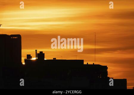 Ciel nuageux spectaculaire au coucher du soleil dans la zone urbaine. Silhouette de bâtiments avec le soleil sur fond jaune et orange Banque D'Images