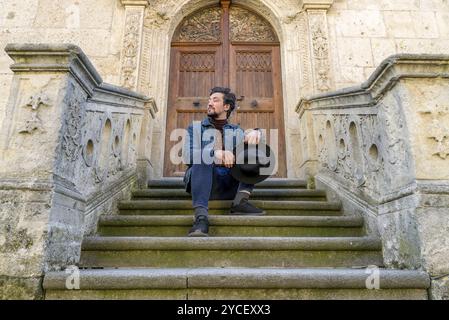 Portrait d'un jeune homme assis contre une belle vieille cathédrale médiévale porte. Un homme en face d'une église architecture une vieille porte d'entrée à Alba Banque D'Images