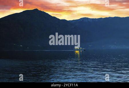 Vue fantastique sur les voiles de bateau illuminé à l'heure bleue sur le lac de Côme d'une côte à l'autre se déplaçant vers la ville de Côme, ciel rose coucher de soleil sur les Alpes italiennes Banque D'Images