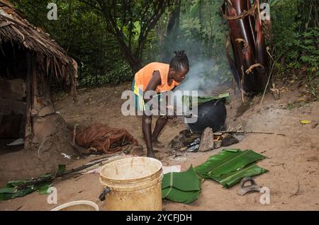 Jeune femme de l'ethnie Ari cuisinant des feuilles de banane farcies dans un pot en terre au-dessus d'un feu ouvert, dans la vallée de l'Omo, Ethiopie Banque D'Images