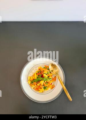 Un repas sans viande de riz cuit avec des légumes servis sur une assiette blanche sur un fond gris Banque D'Images