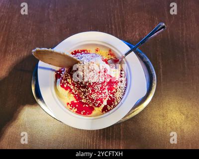 Crème glacée à la vanille avec sauce aux fraises rouges et saupoudrées de chocolat blanc servies dans un bol comme crème glacée à spaghetti avec un cône rond Banque D'Images