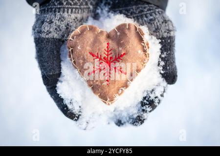 Gros plan de mains gantées tenant un ornement en forme de cœur fabriqué à la main avec un flocon de neige rouge brodé symbolisant l'hiver et la chaleur Banque D'Images